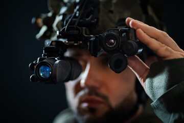 A military man using modern binocular night vision in the darkness. Close up photo.