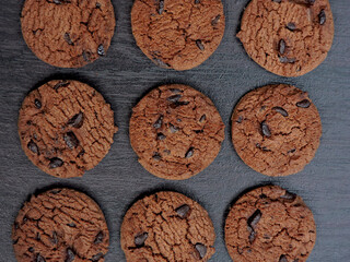 A top-down view of a plate filled with chocolate chip cookies on a dark wooden table. Perfect for themes like food, snacks, desserts