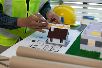 A man is holding a model of a house on a table with other drawings and blueprints. Scene is focused and professional, as the man is likely an architect or engineer working on a project