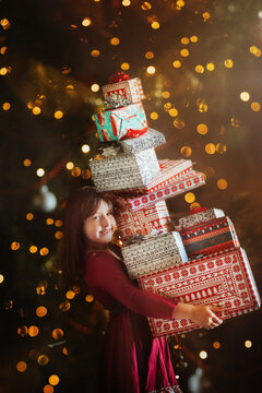 Girl holding stack of gifts standing in front of twinkling lights