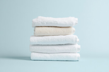 Stack of soft white and beige towels against light blue background