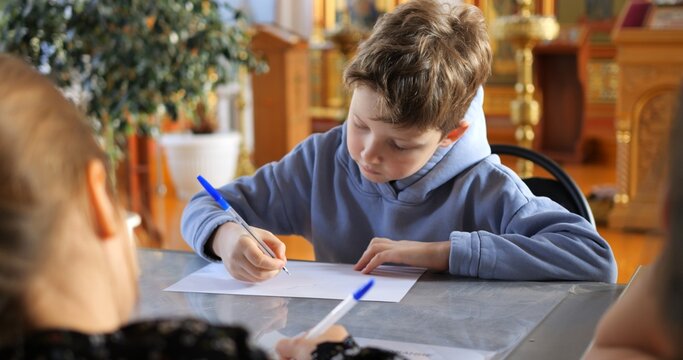 Focused student writing intently during lesson, teacher guiding study inside church interior, highlighting educational commitment within religious learning space. Concept teaching children to write