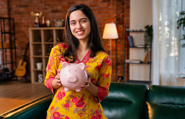 Young Indian woman in kurta showing a piggy bank to emphasise the need for savings and investing