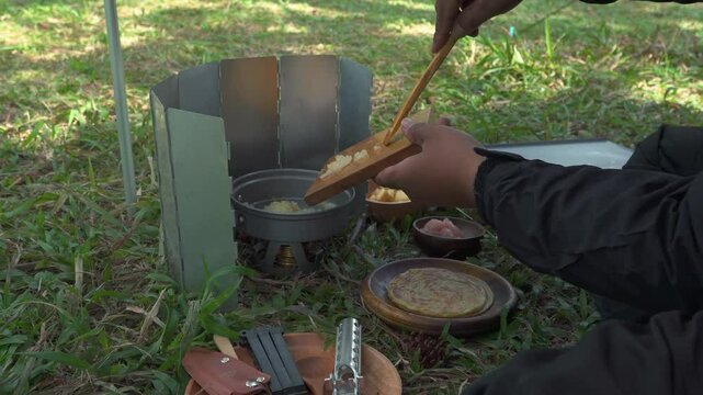 The concept of Bushcraft camping alone in a pine forest area while cooking curry with roti canai. An Asian male adventurer is solo camping while preparing and cooking in beautiful nature