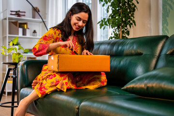 Happy Indian girl in salwar kameez expressing excitement while unboxing a parcel on a sofa