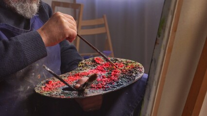 Elder man spending his free time with hobby, visiting art studio class, painting picture with paintbrush on an easel, close up of palette. Daily routine lifestyle concept.