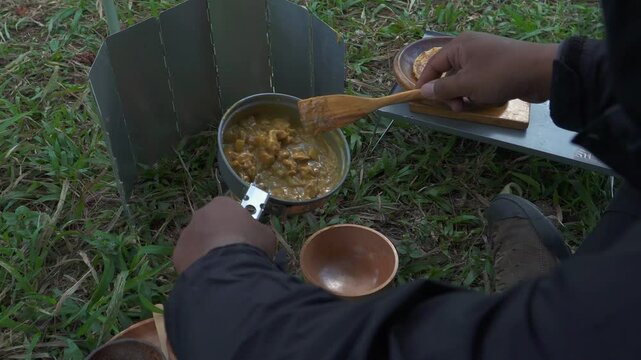 The concept of Bushcraft camping alone in a pine forest area while cooking curry with roti canai. An Asian male adventurer is solo camping while preparing and cooking in beautiful nature