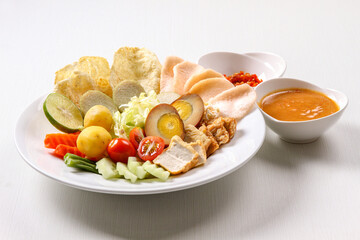 Indonesian gado-gado featuring a variety of vegetables, tofu, tempeh and a hard-boiled egg served with a rich peanut sauce in isolated white background