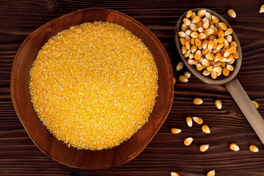Corn grits in a wooden bowl next to dry corn kernels in wooden spoon on a rustic table