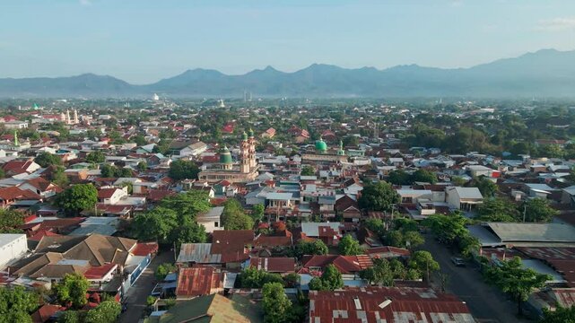 Aerial footage of Lombok, Indonesia known as the '1000 Mosques' town, featuring dense residential areas surrounded by mosques, greenery, and a scenic mountain view.