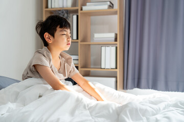 Asian boy sit on bed after wake up in the morning and his eye express asleep feeling with morning...