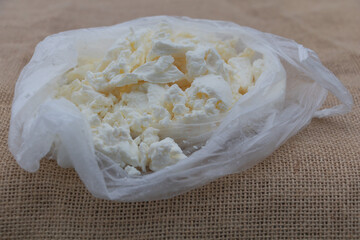A plastic bag of soft white cheese on a burlap background