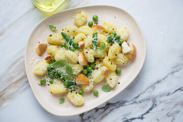 Potato gnocchi with cheese, green peas and basil, horizontal shot on a white stone background, high angle view
