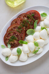 Plate with mini mozzarella balls, sliced tomatoes with basil oil and fresh basil, vertical shot, middle closeup