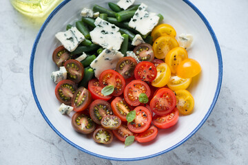 Salad with cherry tomatoes, green beans and blue cheese served in a white and blue plate, horizontal shot, middle closeup