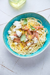 Turquoise bowl with smoked salmon, feta and lemon zest spaghetti, vertical shot on a white granite background, elevated view