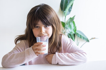 Smiling little child girl drinking a glass of milk in the morning.