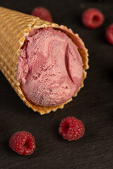 red raspberry ice cream in a waffle cone on a black background