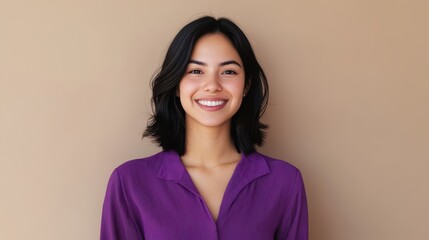 Fototapeta premium Portrait of a smiling Hispanic woman in her 20s with medium-length hair, wearing a purple shirt against a beige background.