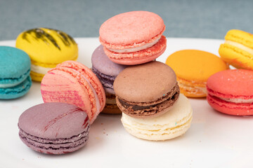 Close up delicious macaroon cookies in fresh mint green vanilla beige chocolate brown orange and pink colors. Light grey background, white plate. Contrast bright combination, bakery culinary.