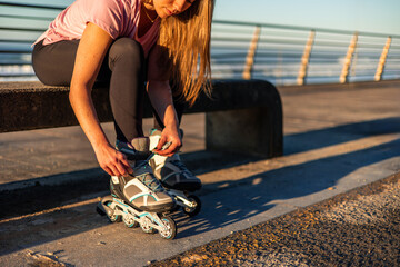 Young sportswoman tying her inline skates sitting on a bench by the sea at sunset copyspace © EDER