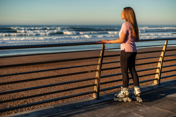 Young woman with inline skates looking at the ocean at sunset from a boardwalk copyspace © EDER