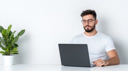 A man working on a laptop at a desk with a plant nearby.