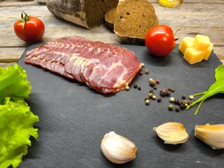 Thin slices of bacon lie on a sliced board