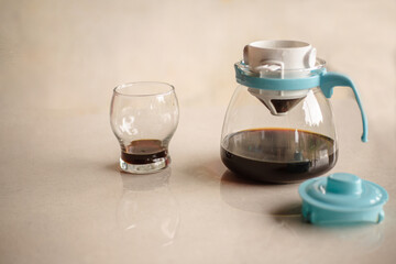 Glass teapot with coffee filter containing filtered black coffee and a glass beside it