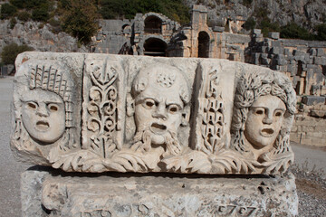 Thre Stone faces of theater performers in the  Ancient Lycian  City of Myra with theater in the background