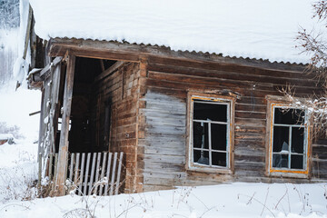 There is an old wooden house standing quietly, its roof and windows covered in a thick layer of snow, creating a serene and picturesque winter scene that is truly enchanting