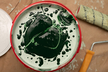 Green paint in a red bucket, ready for application with a roller, ideal for interior painting projects and renovation activities, captured in detailed, artistic manner. White paint and green dye