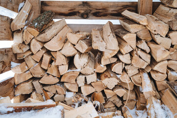 A large, neatly arranged pile of logs stacked meticulously on top of each other, resting in a blanket of soft white snow, creating a striking contrast between the wood and the cold surface