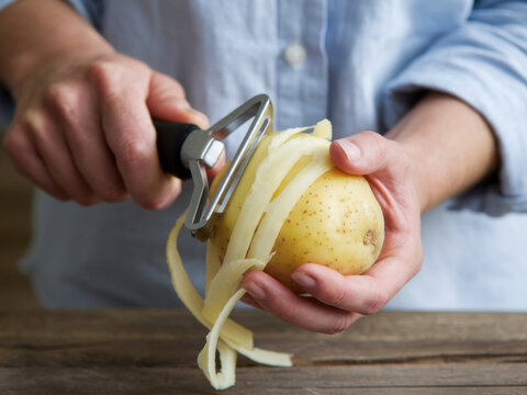 Cerca de las manos pelando una patata con un pelador de patatas
