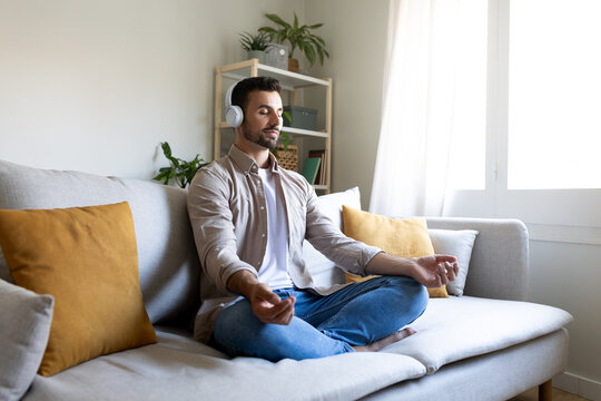 Man meditating on the couch listening to guided meditation using wireless headphones.