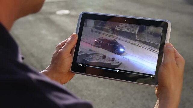 A man, perhaps on vacation, watches his security camera as a car slides down the street outside his home.	
