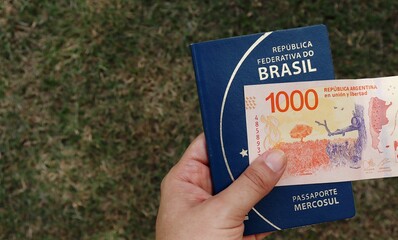 Person holding brazilian passport and 1000 pesos argentinos. Brazilians travelling to Argentina concept. 