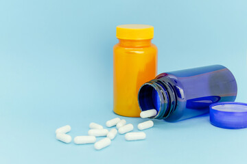 Yellow and blue bottle and scattered white capsules on light blue background. Space for text