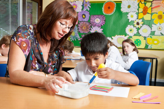 Elementary School: Arts and Crafts. A young boy of South Asian Indian heritage having some help with his class project from his teacher in the classroom.