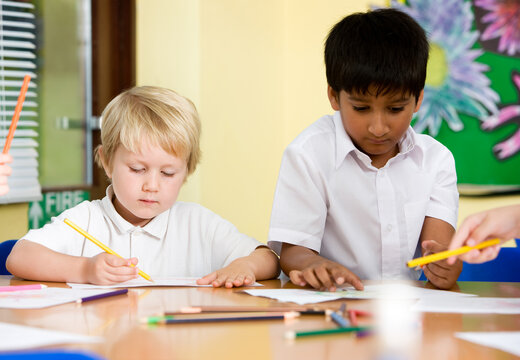 Elementary School: Early Learning. A candid moment between a pair of young primary school pupils in class working on a creative art project.
