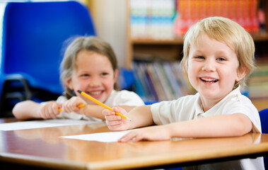 Elementary School: Candid and Carefree. A carefree and candid moment between a pair of young primary school friends sitting at their desk in the classroom.
