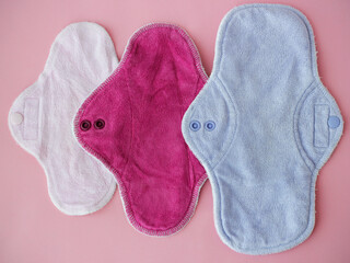 Three bamboo washable sanitary napkins in different sizes on pink background. Colorful eco reusable...