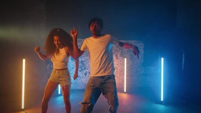 Dancers dancing in studio, attractive black woman and man, full-length shot. Pair of dancers immersed in creative flow, performing intricate modern choreography to upbeat tracks in rehearsal area