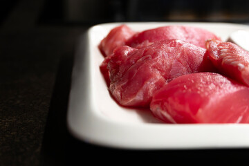 Sliced raw tuna fish on white rectangular plate on black table, fish steaks close-up
