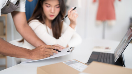 A man and woman work together to verify orders on paper and laptop in an online business workspace