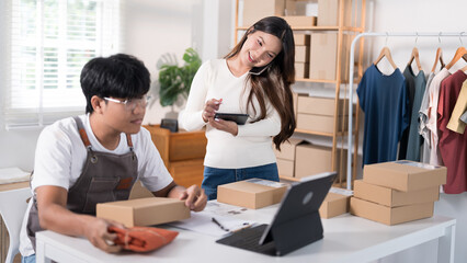 A woman uses a tablet to take photos of a product while a man organizes boxes in the background