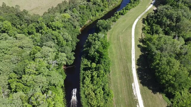Drone view of a boat going through river in agricultural field on a sunny day in Ocala City, Florida