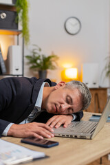 Bored sleepy businessman working on laptop computer leaning on hand sleeps at home office desk....