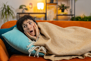 Young Caucasian woman suddenly wakes up from nightmare while sleeping on couch due to anxiety,...