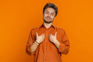I am the best, choose me. Happy Caucasian man feeling very proud pointing himself, looking self-confident, overjoyed by success, making choice. Young guy isolated on studio orange background indoors
